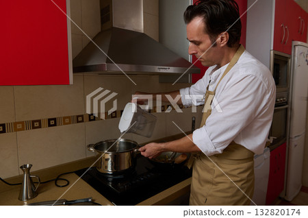 Man In Apron Cooking Soup In Modern Kitchen While Pouring Water For Dinner 132820174