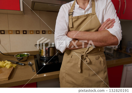 Chef In Apron Standing With Arms Crossed In Kitchen Over Pot And Chopped Potatoes 132820191