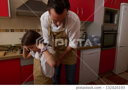 Father And Daughter Cooking Together In A Modern Kitchen, Wearing Aprons, Preparing Dinner Father And Daughter Cooking Together In A Modern Kitchen, Wearing Aprons, Preparing Dinner 132820193