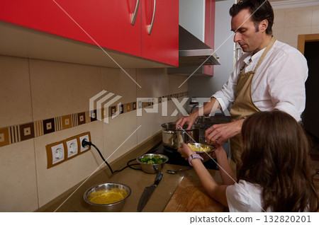 Father Cooking Soup in Kitchen While Daughter Helps Serve Dinner Father Cooking Soup in Kitchen While Daughter Helps Serve Dinner 132820201
