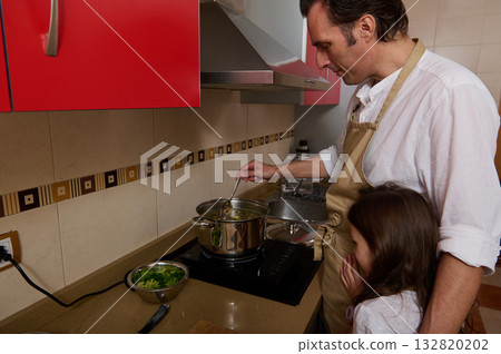 Father Cooking Soup On Stove While Daughter Watches And Helps In Kitchen 132820202