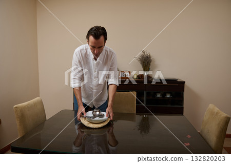 Man In White Shirt Sets Dinner Table In Minimal Dining Room 132820203