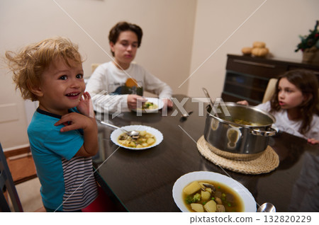 Family Dinner: Three Kids At The Kitchen Table Sharing Soup From A Pot 132820229