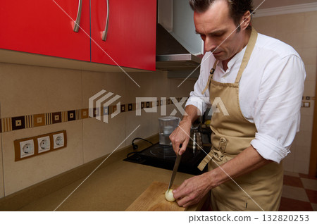 Man Cooking Onion In Apron In Modern Kitchen, Chopping Onions For Dinner Man Cooking Onion In Apron In Modern Kitchen, Chopping Onions For Dinner 132820253