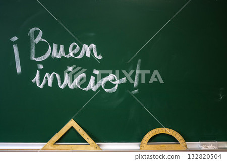 Spanish phrase Buen inicio written on green classroom chalkboard with math tools 132820504