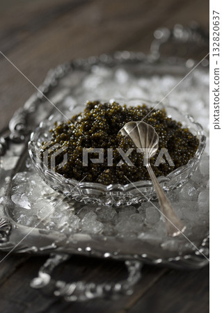 Black caviar with a spoon on ice. High-quality natural sturgeon black caviar close-up. Delicacy. Texture of expensive luxury caviar on metal tray. Black caviar with a spoon on ice. High-quality natural sturgeon black caviar close-up. Delicacy. Texture of expensive luxury caviar on metal tray. 132820637