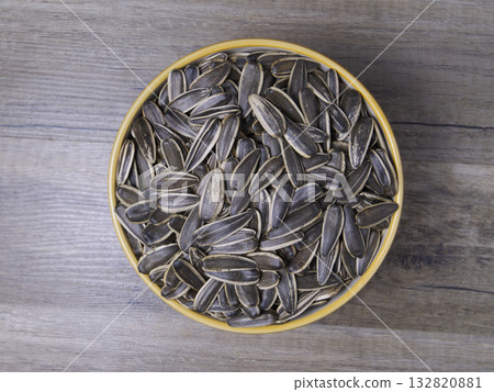 Striped sunflower seeds in a bowl on a wooden table. 132820881