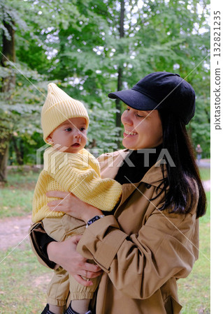 Mother Holding Baby in Yellow Outfit at Park 132821235
