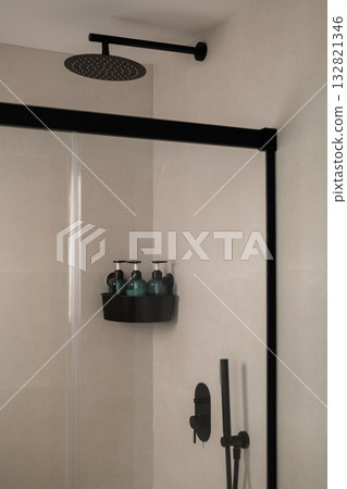 Modern shower with a black showerhead and glass enclosure. A shelf holds several green bottles. The walls are light-colored and minimalistic. Modern shower with a black showerhead and glass enclosure. A shelf holds several green bottles. The walls are light-colored and minimalistic. 132821346