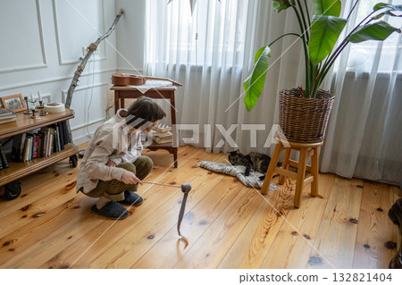Young woman activating lazy cat on floor. Playful stimulation for healthy feline instinct play Young woman activating lazy cat on floor. Playful stimulation for healthy feline instinct play 132821404