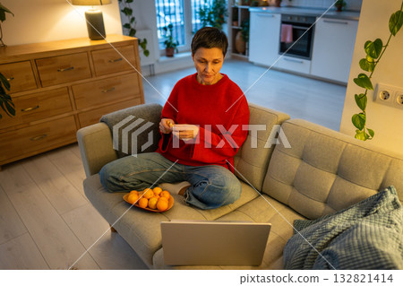 Relaxed mature woman watching movie. Content female eating mandarin laptop sofa, Downtime with snack Relaxed mature woman watching movie. Content female eating mandarin laptop sofa, Downtime with snack 132821414