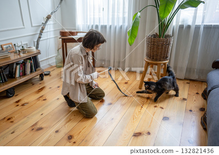 Amused woman owner engages cat in lively interactive game at home. Healthy pet playtime activity 132821436