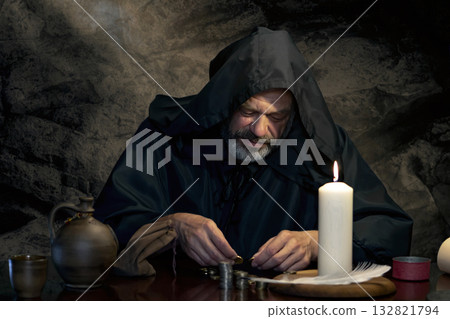 A hooded man is concentrating on counting money on a wooden table. A hooded man is concentrating on counting money on a wooden table. 132821794