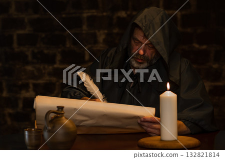 A medieval monk writes with a quill pen on parchment by candlelight. A medieval monk writes with a quill pen on parchment by candlelight. 132821814