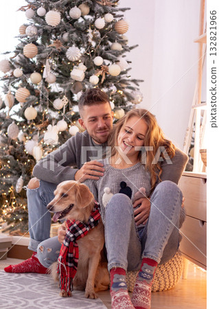 Happy couple and their dog sit by a glowing Christmas tree. The image captures love warmth and the joyful spirit of the holidays. Happy couple and their dog sit by a glowing Christmas tree. The image captures love warmth and the joyful spirit of the holidays. 132821966