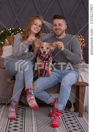 Happy Couple and Dog Enjoy Festive Winter Christmas Moments Together. The image celebrates love, joy and the warmth of the holiday season at cozy home. 132821967