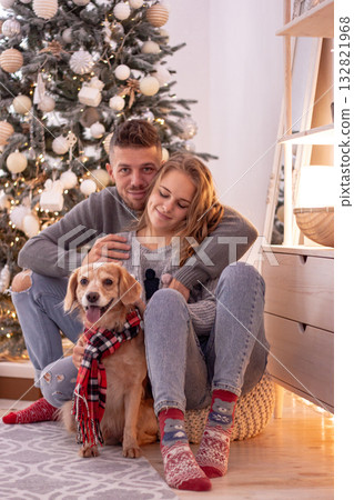 Couple and their dog relax in a cozy Christmas home. The scene embodies love comfort and the joyful spirit of the holiday season. 132821968