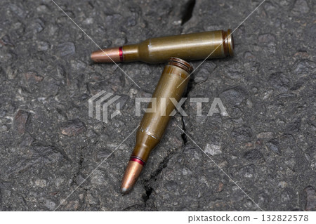 Two cartridges with a bullet with an offset center lies on a dark textural background, selective focus, Concept:prohibited expansive bullets, the war in Ukraine. 132822578