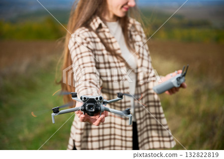 A young woman stands in a beautiful, open field, excitedly holding a drone in one hand and a remote control in the other, ready to capture stunning aerial views. A young woman stands in a beautiful, open field, excitedly holding a drone in one hand and a remote control in the other, ready to capture stunning aerial views. 132822819