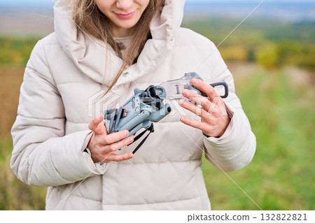 A woman in a cozy jacket inspects her drone while standing in a colorful landscape filled with autumn foliage. The sky is bright and clear, showcasing a serene environment. A woman in a cozy jacket inspects her drone while standing in a colorful landscape filled with autumn foliage. The sky is bright and clear, showcasing a serene environment. 132822821