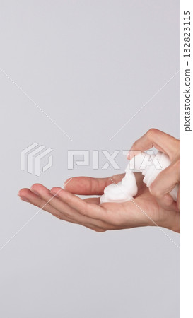 Young woman applying hand foam soap or foam to wash face, skin care, cleansing, hygiene, health care ads. Finger presses taking foam from bottle. Close-up palm of hands on isolated grey background Young woman applying hand foam soap or foam to wash face, skin care, cleansing, hygiene, health care ads. Finger presses taking foam from bottle. Close-up palm of hands on isolated grey background 132823115