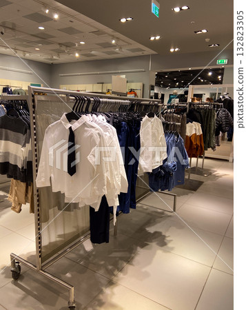 Stylish retail space with organized clothing racks displaying children shirts, trousers, and sweaters under bright lights. Fashion retail, modern presentation, and seasonal shopping. Stylish retail space with organized clothing racks displaying children shirts, trousers, and sweaters under bright lights. Fashion retail, modern presentation, and seasonal shopping. 132823305