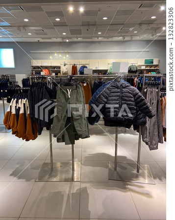 Modern children retail display with racks of outerwear, pants, and sweaters in neutral and earthy tones. Seasonal fashion, shopping atmosphere, and commercial retail design. 132823306