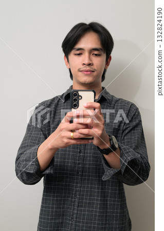 Portrait of handsome Young Asian Thai man using phone against white background Portrait of handsome Young Asian Thai man using phone against white background 132824190
