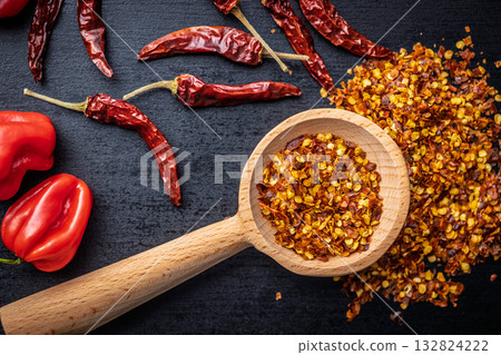 Red chili peppers flakes. Milled spicy peppers on wooden scoop on black table. Top view. 132824222