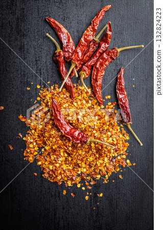 Red chili peppers flakes. Milled spicy peppers on black table. Top view. Red chili peppers flakes. Milled spicy peppers on black table. Top view. 132824223