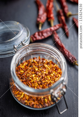 Red chili peppers flakes. Milled spicy peppers in jar on black table. 132824230