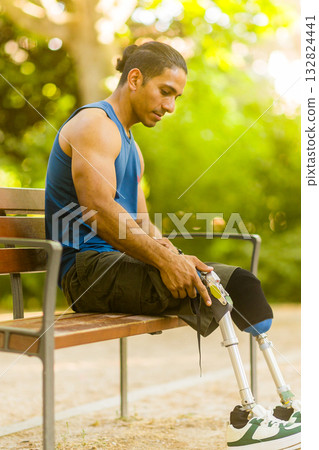 Disabled athlete adjusting prosthetic legs on park bench 132824441
