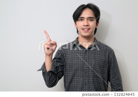 Portrait of handsome Young Asian Thai man pointing finger against white background Portrait of handsome Young Asian Thai man pointing finger against white background 132824645