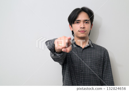 Portrait of handsome Young Asian Thai man pointing finger against white background Portrait of handsome Young Asian Thai man pointing finger against white background 132824656