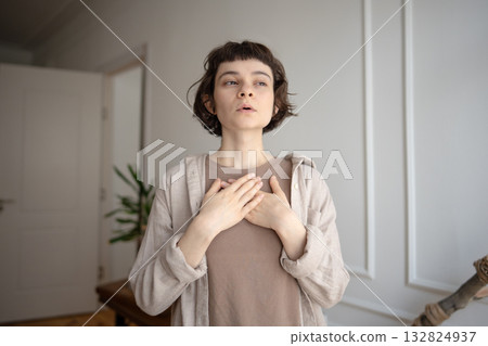 Young woman practicing stress relief, doing breathing exercises for calming, holding hands on chest. Young woman practicing stress relief, doing breathing exercises for calming, holding hands on chest. 132824937