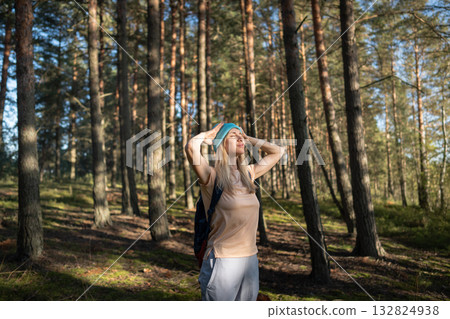 Serene female meditating hands behind head taking deep breaths with closed eyes under forest sun Serene female meditating hands behind head taking deep breaths with closed eyes under forest sun 132824938
