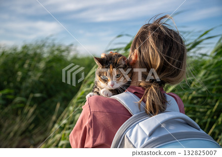 Woman walking outdoors exploring nature on windy day with her domestic cat, carrying animal in hands Woman walking outdoors exploring nature on windy day with her domestic cat, carrying animal in hands 132825007