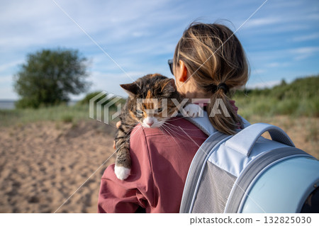 Woman pet owner hiking exploring nature on sunny day with her domestic cat, carrying animal in hands Woman pet owner hiking exploring nature on sunny day with her domestic cat, carrying animal in hands 132825030