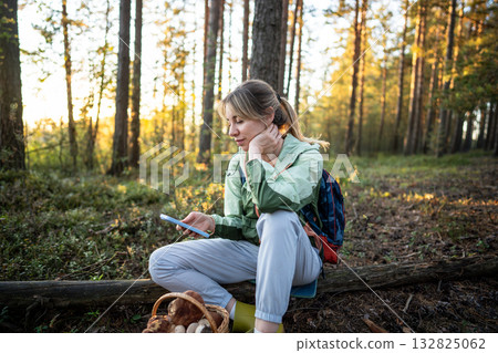 Joyful happy woman checking smartphone and planning route after mushroom foraging in forest Joyful happy woman checking smartphone and planning route after mushroom foraging in forest 132825062