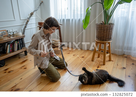 Happy woman spending weekend time home with pet, playing on floor with domestic cat in living room. 132825072