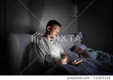 Man with phone in bed, feel procrastination at night. Struggling with insomnia in dark bedroom 132825120