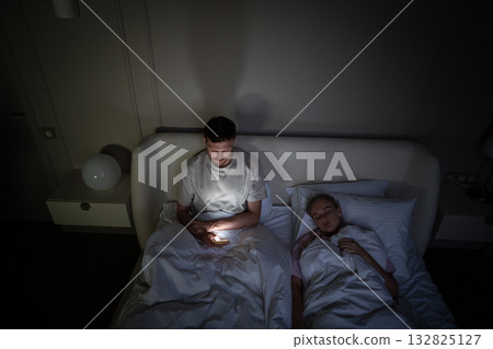 Exhausted man awake alone in bed scrolling phone due to insomnia and digital addiction on late hours Exhausted man awake alone in bed scrolling phone due to insomnia and digital addiction on late hours 132825127