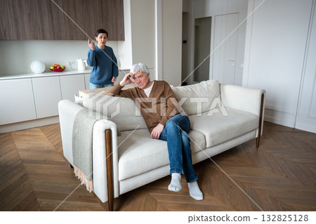 Irritated wife criticizes exhausted husband slumped on sofa for failing to help, passive partner 132825128