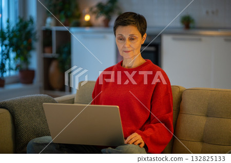 Tranquil mature woman work calmly on laptop on sofa in comfortable living room. Female productivity 132825133