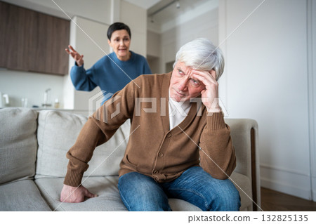 Furious wife shouts at husband while he wearies from relentless criticism on sofa. Nagging stress 132825135