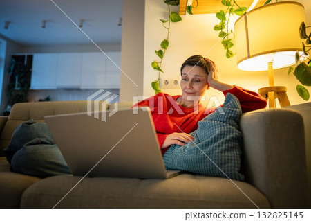 Smiling happy woman sprawl on couch watching movies on laptop in cozy living room alone, female rest 132825145