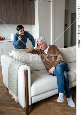 Frustrated wife berates weary husband lounging on couch over neglected duties. Old couple conflict 132825152