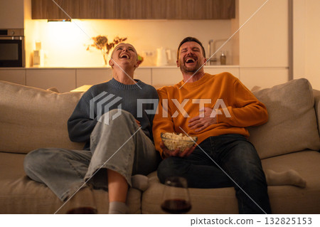 Laughing couple watch TV comedy with popcorn at night. Home theater entertainment in family Laughing couple watch TV comedy with popcorn at night. Home theater entertainment in family 132825153