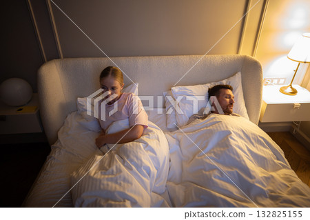 Unhappy sleep deprived woman lying awake in bed due to husband snoring in shared bedroom, insomnia Unhappy sleep deprived woman lying awake in bed due to husband snoring in shared bedroom, insomnia 132825155