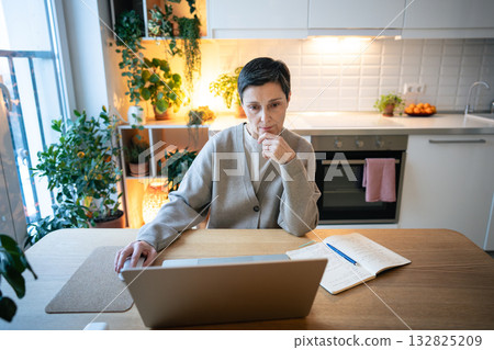 Thoughtful woman types on laptop in kitchen, searching solutions. Balancing deadlines, remote work Thoughtful woman types on laptop in kitchen, searching solutions. Balancing deadlines, remote work 132825209